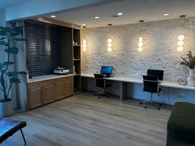 Modern office workspace with two desks, office chairs, built-in wood cabinetry, and stone accent wall