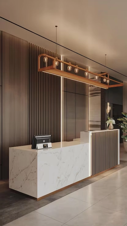 White marble reception desk with POS system monitor under linear modern lighting in a lobby.