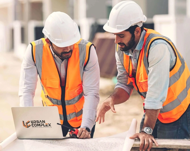 Two Urban Complex construction engineers discussing building plans on a laptop